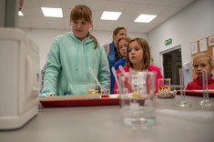 Na pierwszym planie znadują się dzieci biorące udział w eksperymencie w laboratorium.
